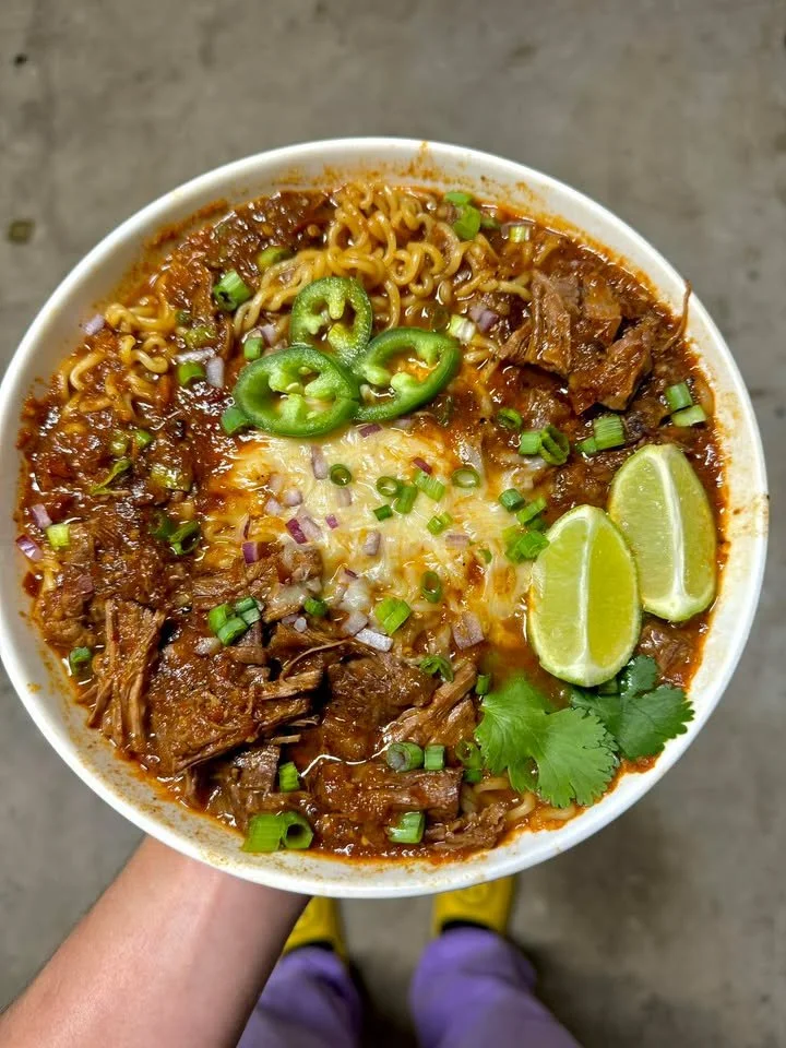 A bowl of Birria Ramen topped with tender beef, herbs, and chili broth.