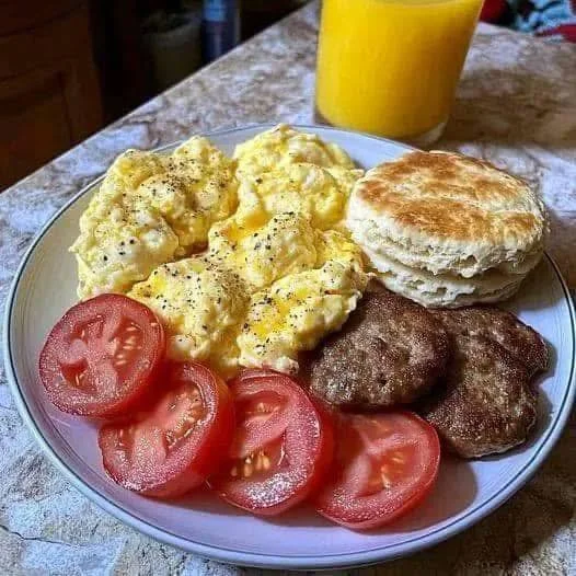 Breakfast feast with scrambled eggs, sausage patties, biscuits, and tomatoes