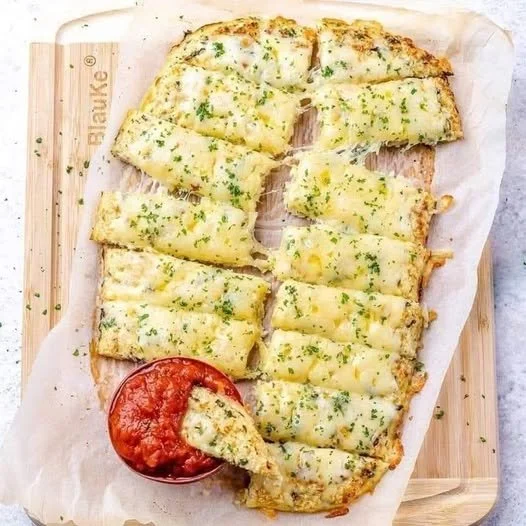 Cheesy cauliflower breadsticks served on a plate with dipping sauce.