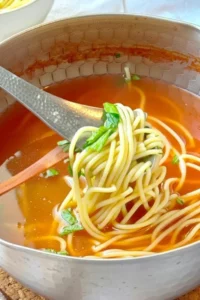 A bowl of homemade chicken broth garnished with herbs.