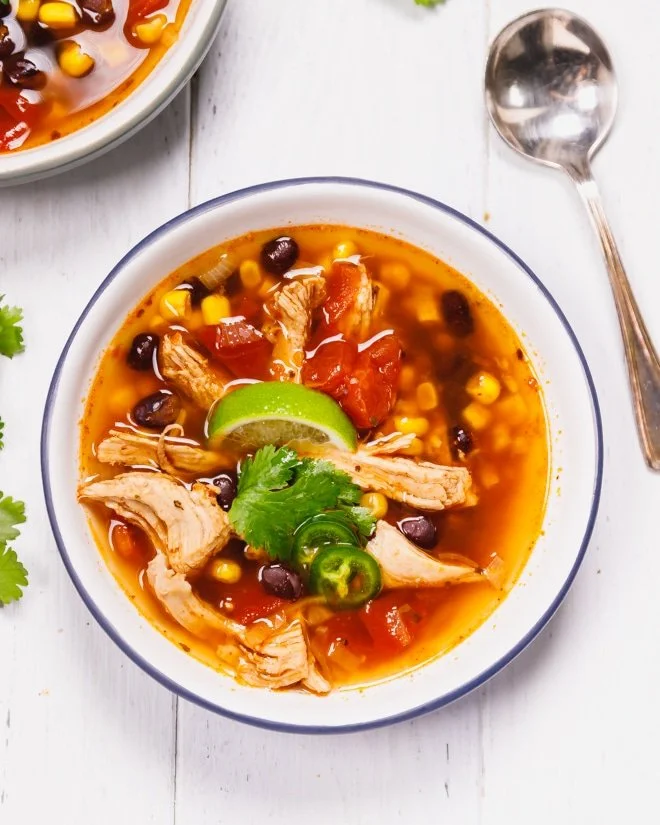 Bowl of homemade Chicken Tortilla Soup topped with crispy tortilla strips and avocado.