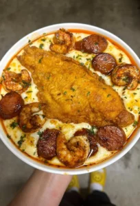 Fried catfish served with shrimp and sausage cheddar grits on a plate