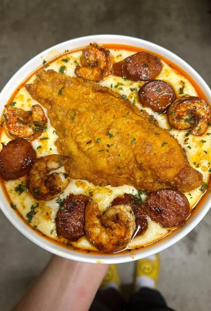 Fried catfish served with shrimp and sausage cheddar grits on a plate