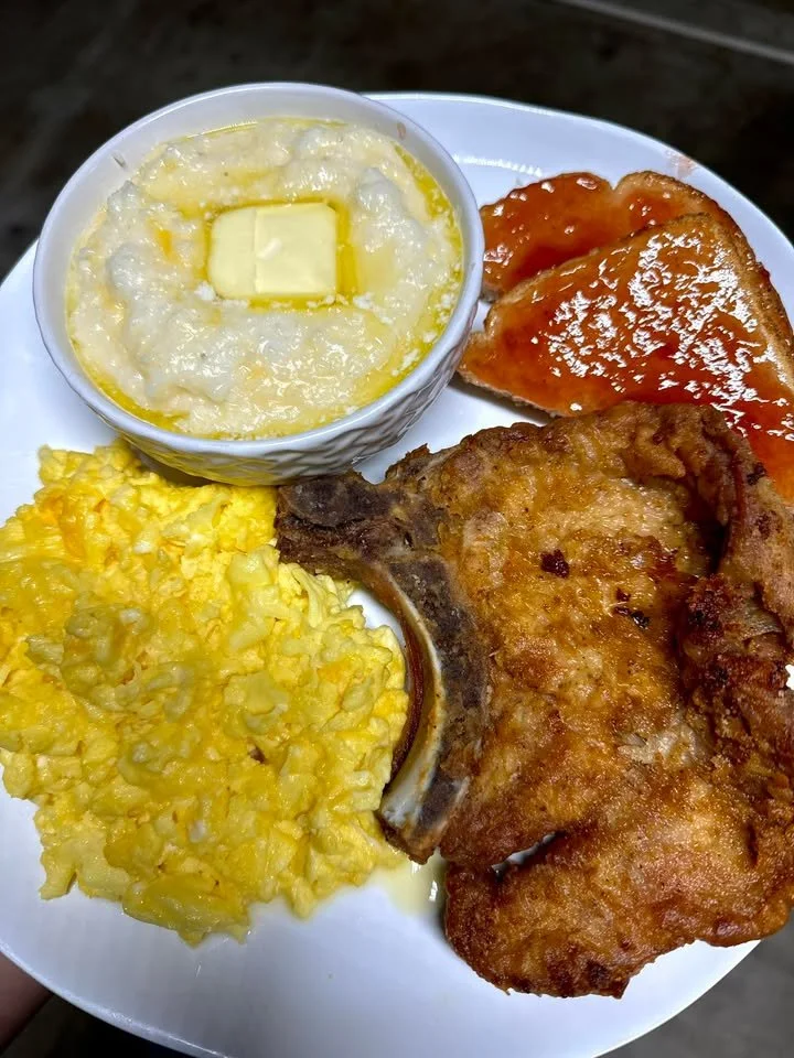 Fried pork chop with scrambled eggs, grits, and jelly toast served on a plate.