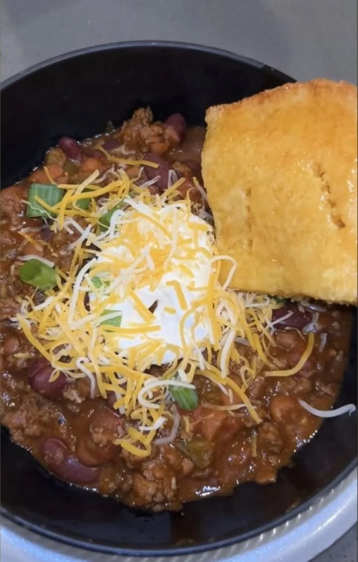 Homemade chili cornbread served in a bowl, topped with cheese and herbs.