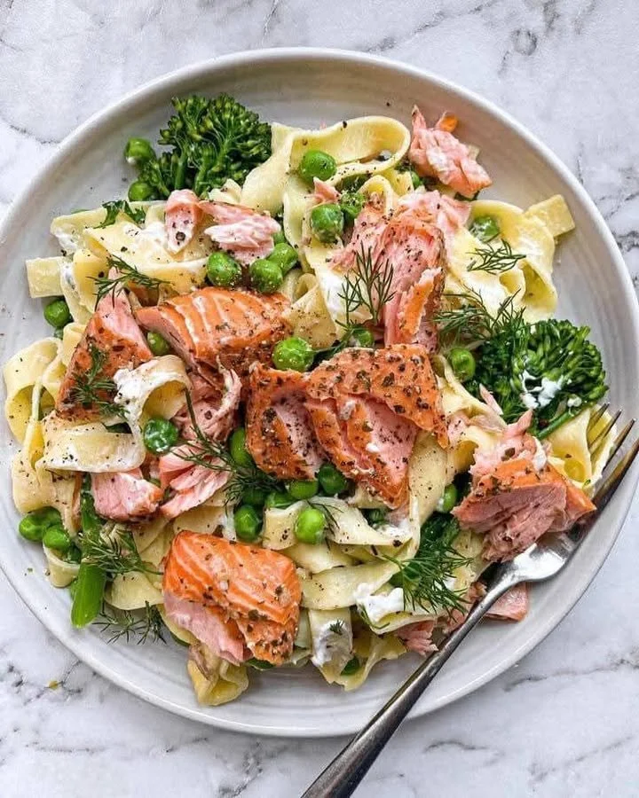 Plate of hot smoked salmon tagliatelle topped with fresh greens