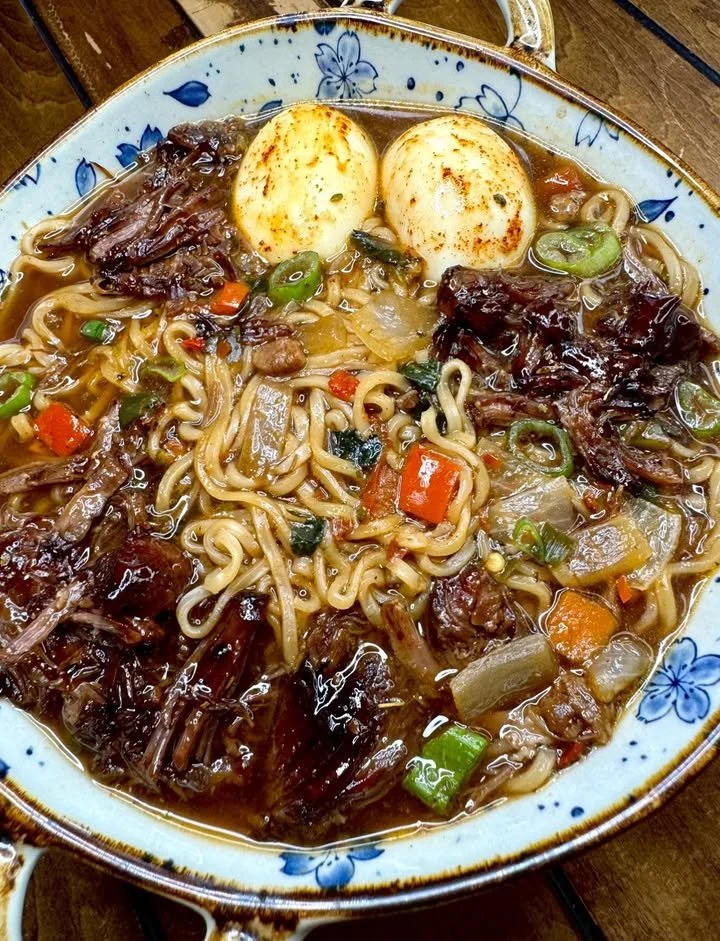 A bowl of jerk oxtail ramen garnished with green onions and herbs.