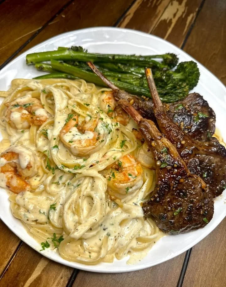 Lamb Alfredo dish with shrimp, creamy sauce, and garnish on a plate.