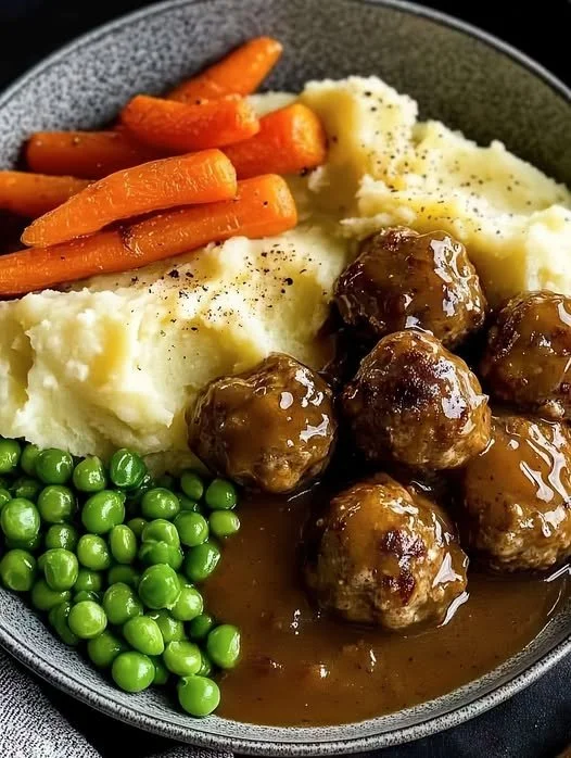 Plate of meatballs served with mashed potatoes, gravy, carrots, and peas