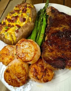 Plate of New York Strip steak with scallops, garnished for a gourmet meal.