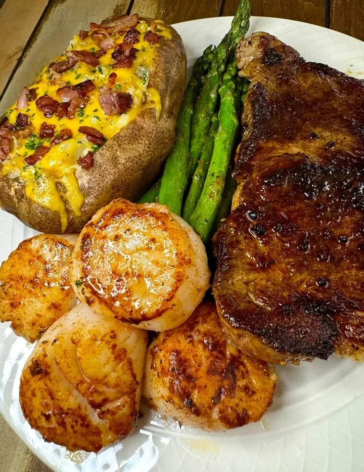 Plate of New York Strip steak with scallops, garnished for a gourmet meal.
