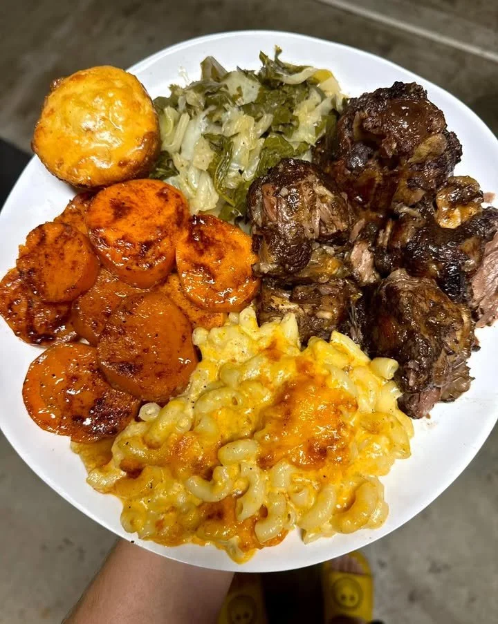 Delicious oxtail plate with mixed greens, candied sweet potatoes, and baked macaroni.