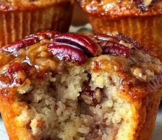 Pecan pie muffins topped with caramel drizzle and crushed pecans on a wooden table.