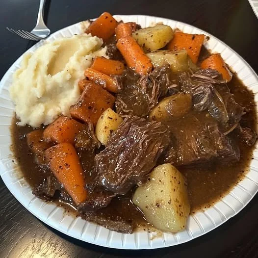 Delicious pot roast served with carrots, potatoes, and gravy in a rustic setting.