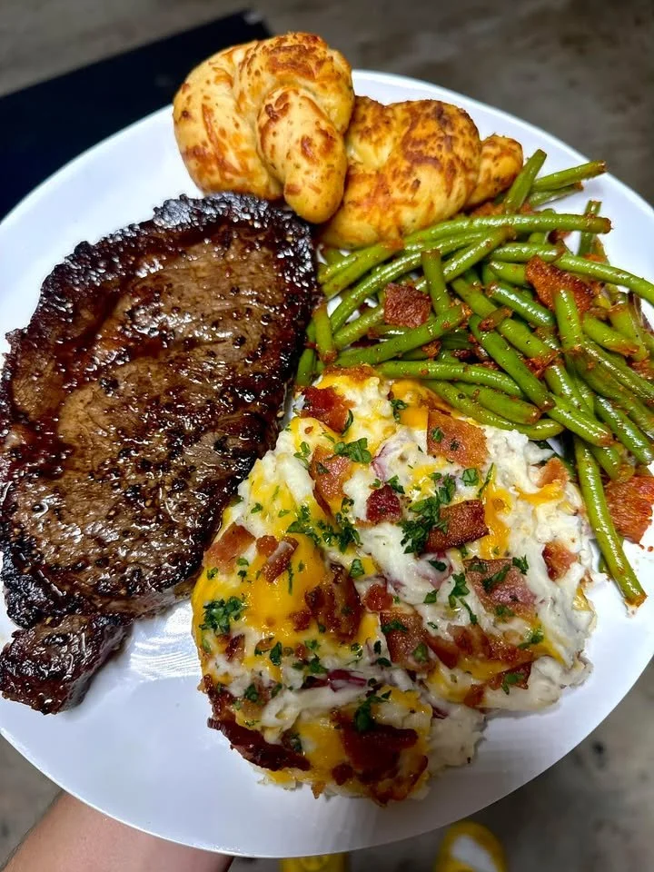 Ribeye steak served with loaded red skin mashed potatoes, garlic knots, and green beans