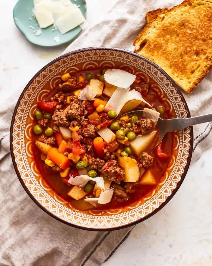 Bowl of savory hamburger vegetable soup garnished with fresh herbs.