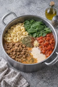 A steaming bowl of creamy tortellini soup garnished with basil and cheese.