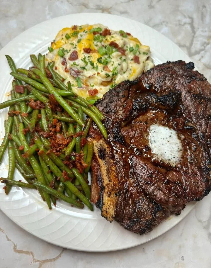 Smoked ribeye steak served with loaded mashed potatoes and green beans on a plate.