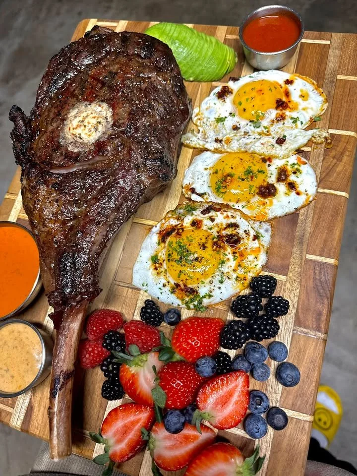 Smoked Tomahawk steak served on a board with fried eggs, showcasing a hearty meal.
