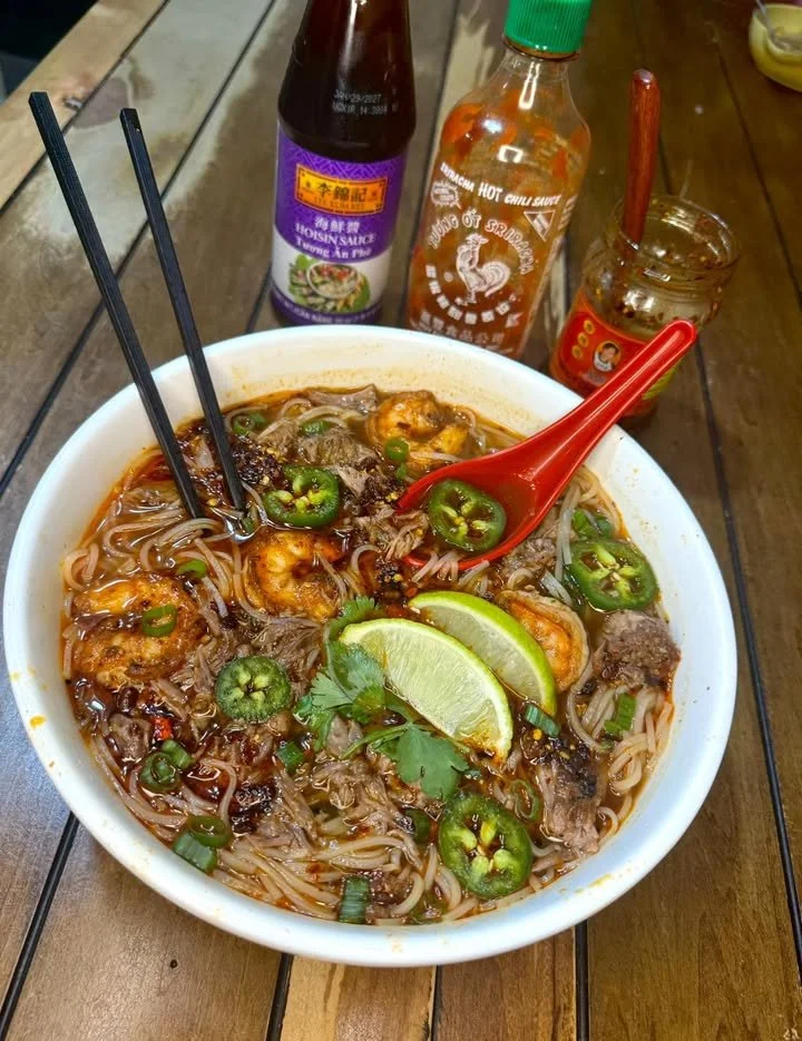 Bowl of spicy oxtail and shrimp pho garnished with fresh herbs and lime.
