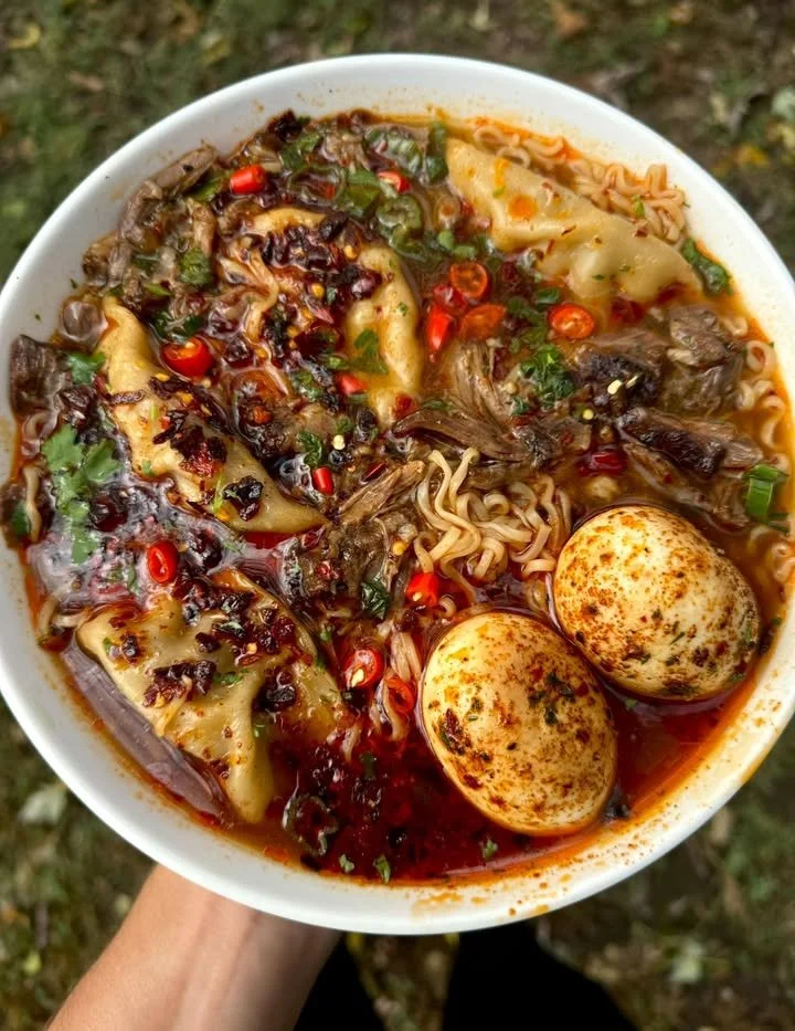 Bowl of spicy oxtail dumpling and noodle soup garnished with herbs