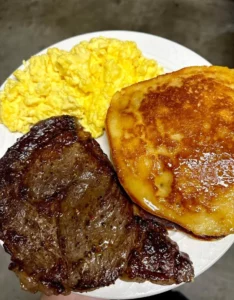 Delicious steak, scrambled eggs, and pancakes served on a plate