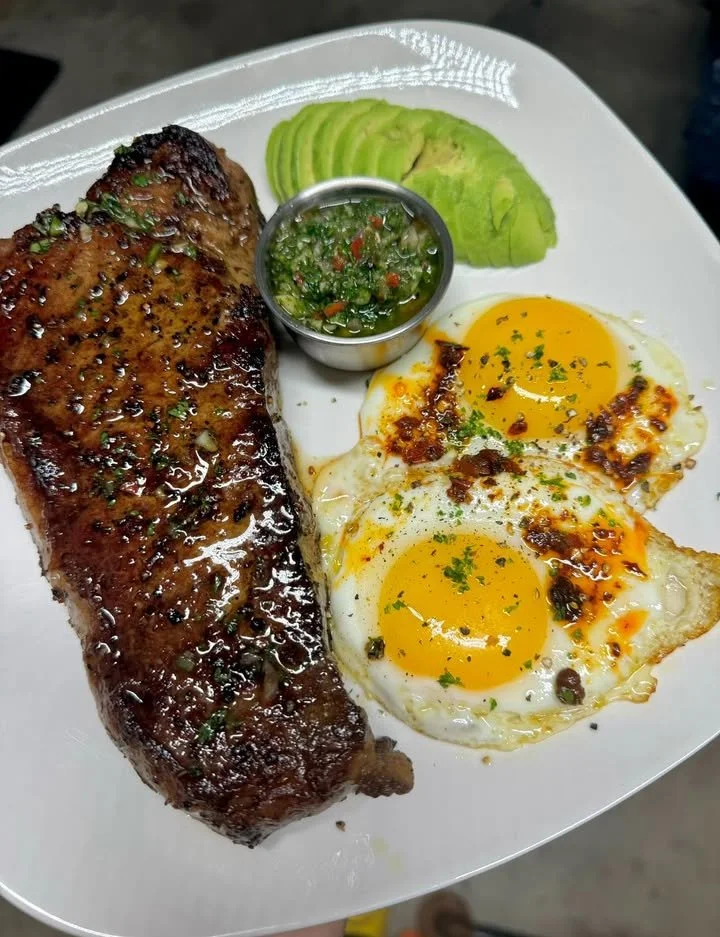 Delicious strip steak topped with fried eggs and avocado on a plate.