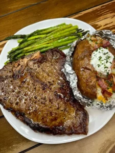 Juicy T-Bone steak served with a loaded baked potato and asparagus on a plate.