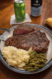 Delicious T-Bone steak served with potatoes, green beans, and a biscuit.