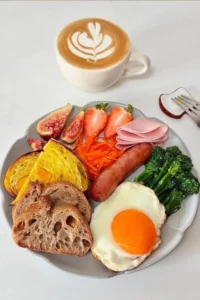 A colorful breakfast platter with eggs, fruits, and pastries on a wooden table.