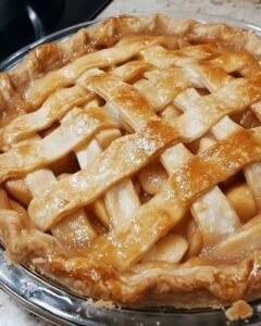 A beautifully baked classic apple pie with a golden crust and apple filling on a wooden table.