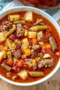 A bowl of hearty vegetable beef soup with fresh vegetables and tender beef chunks.